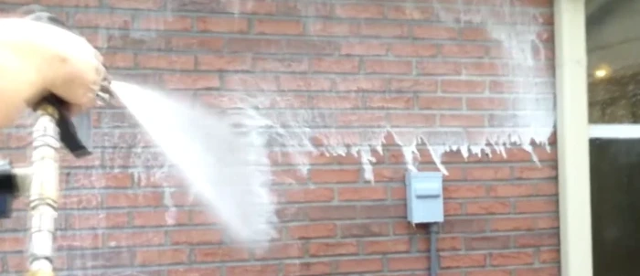 Pressure washer wand rinsing a red brick exterior wall