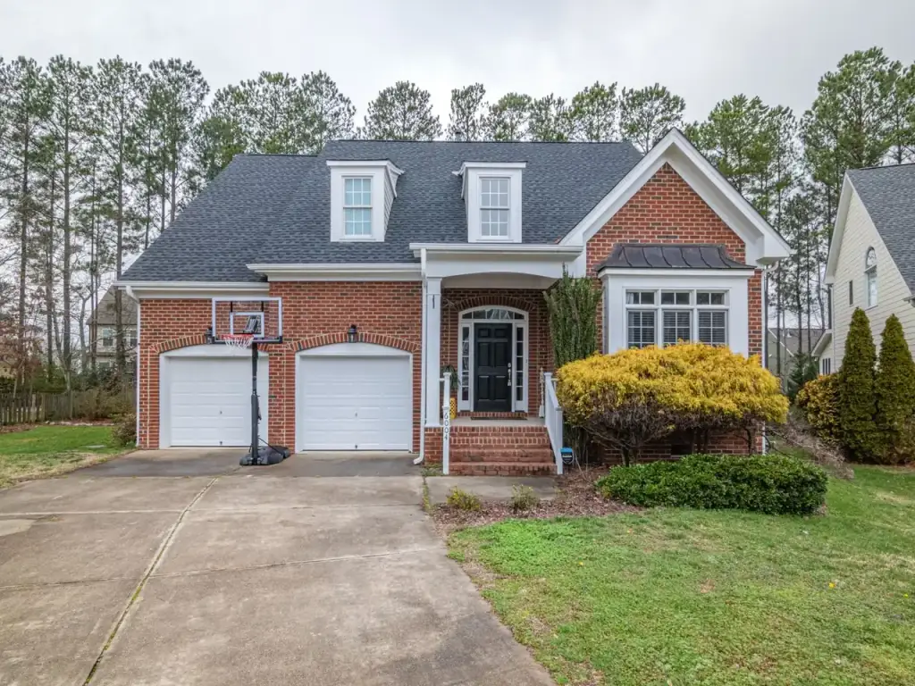 Brick house with a steep shingle roof, dormers and a garage