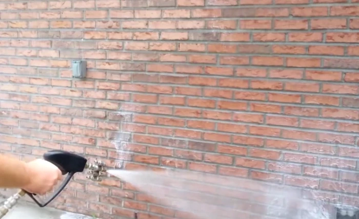Water spraying from a pressure washer nozzle across brick