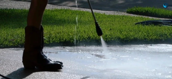 Pressure washing a concrete driveway beside a lawn