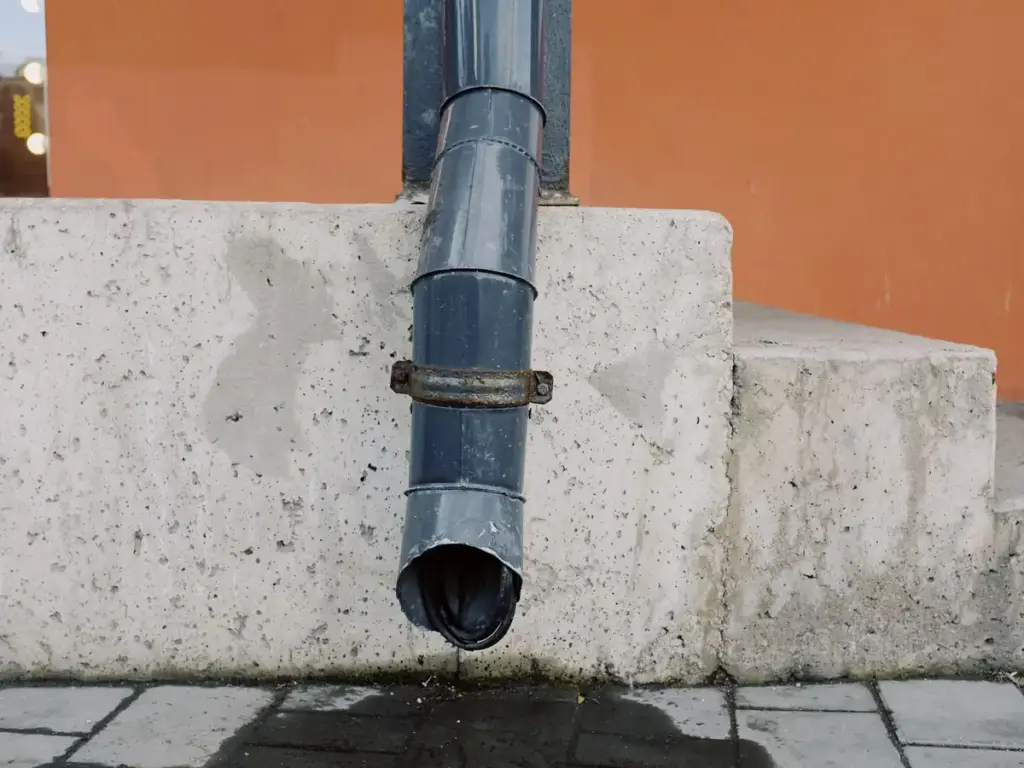 Grey downspout ending above paving beside concrete steps