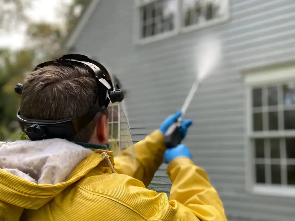 Worker in a rain jacket washing the lap siding of a house with a spray wand