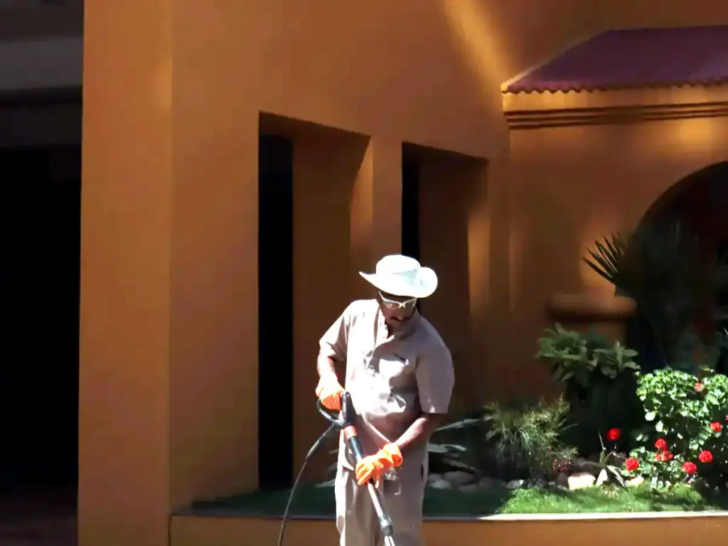Gardener pressure washing a walkway beside a building