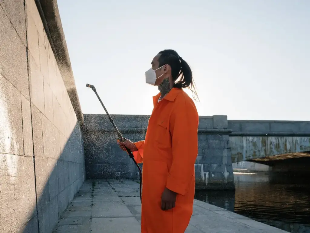 Worker in orange coveralls pressure washing a concrete wall